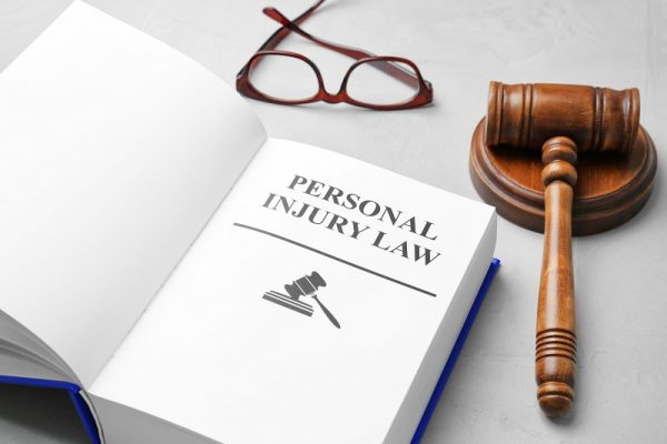 Book with words PERSONAL INJURY LAW, gavel and glasses on grey b