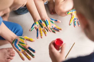 teacher works with children according to the Montessori method and paints their hands. Kindergarten teacher therapy session with children with autism spectrum disorder.